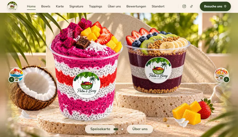 Startseite von Palm & Berry am Bildschirm: A&ccedil;a&iacute;-Bowls auf Travertin-Podesten zwischen Palmbl&auml;ttern, die Szene bewegt sich in der Tiefe